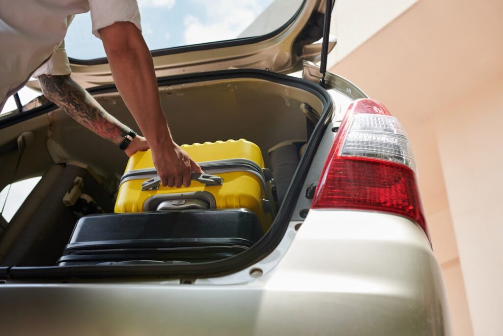 tattooed man putting suitcase into taxi for airport transfer